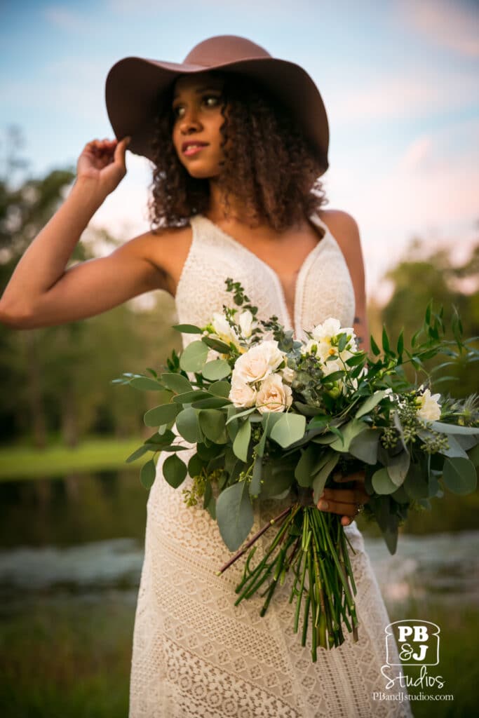 bride in a large sunhat standing outside holding her large flower bouquet